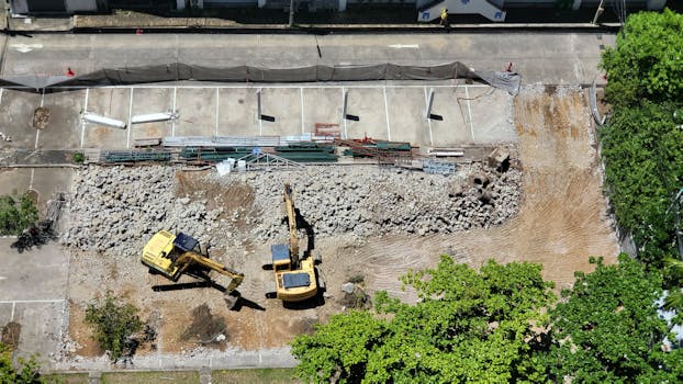 Aerial shot of an urban construction site with excavators moving debris and dirt.